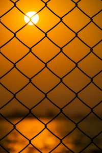 Full frame shot of chainlink fence against sky during sunset