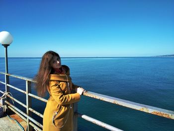 Beautiful woman standing by railing on pier against sea