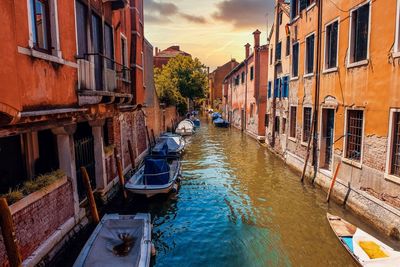 Boats moored in canal amidst buildings against sky