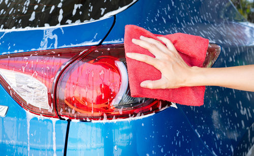 Car wash service. car covered with white soap foam. man hand holding red microfiber cloth and polish