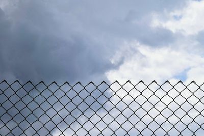 Low angle view of chainlink fence against cloudy sky