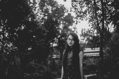 Portrait of smiling young woman standing against trees