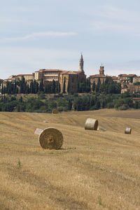 Hay bales on field by building against sky