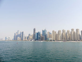 Sea by modern buildings against clear sky