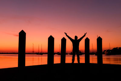 Silhouette man by sea against sky during sunset