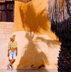 Woman wearing hat standing against wall outdoors