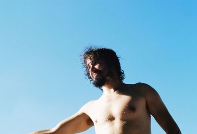 Low angle view of shirtless man standing against clear blue sky