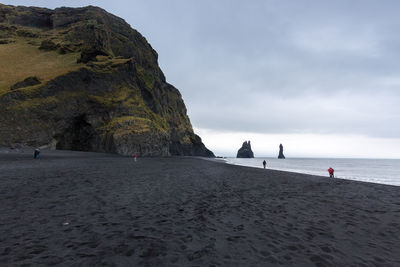 Scenic view of cliff by beach against cloudy sky at dyrholaey