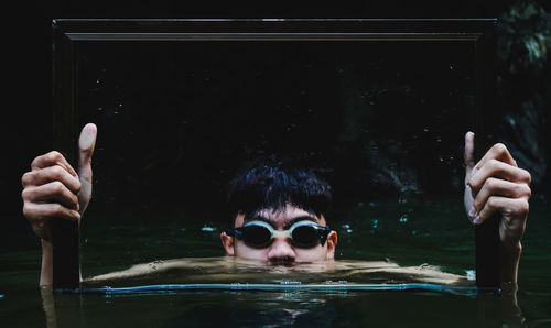 Shirtless young man holding frame while swimming in lake