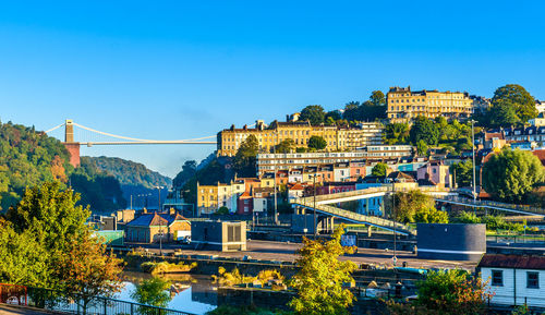 Bridge over river by buildings against clear blue sky