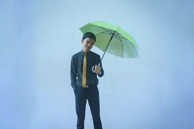 Portrait of young man holding umbrella while standing over blue background