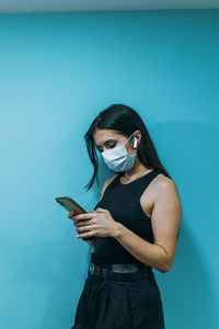 Young woman using mobile phone against blue wall