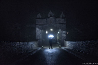 Rear view of man standing on illuminated road at night