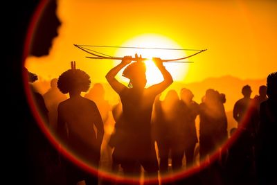 Silhouette people performing seen through lens flare against orange sky