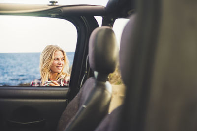 Beautiful woman smiling against sea seen through car window