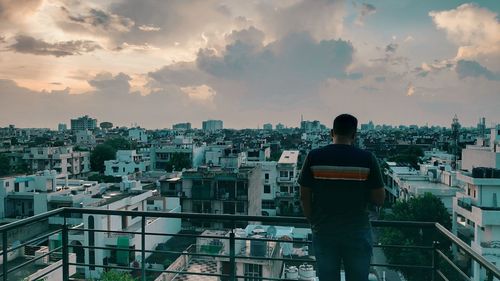 Rear view of man standing by railing against sky during sunset