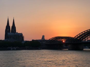 Bridge over river by buildings against sky during sunset