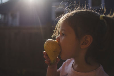 Close-up of girl eating pear while standing in backyard during sunset