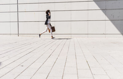 Businesswoman with briefcase running while telephoning with smartphone