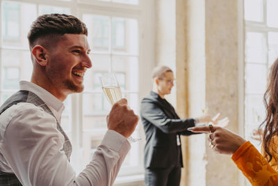 Side view of smiling businessman drinking white wine during event at convention center