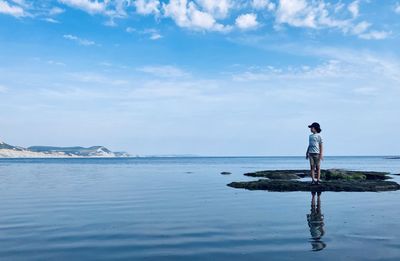 Full length of boy standing on rock against sea and sky