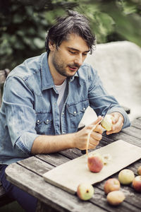 Mid adult man peeling apples at table in organic farm