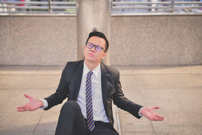 Businessman gesturing while sitting on walkway