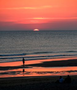 Silhouette man standing on beach against orange sky