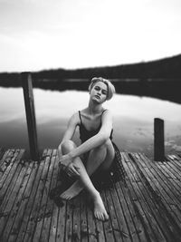 Portrait of teenage girl sitting on pier over lake against sky