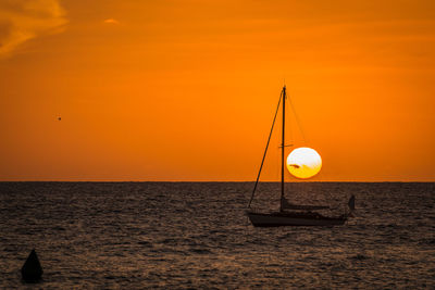 Silhouette boat on beach against orange sky