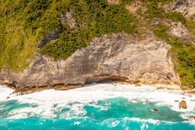 High rocks with green tropical vegetation, foamy sea water. drone type. bali, klungkung, indonesia