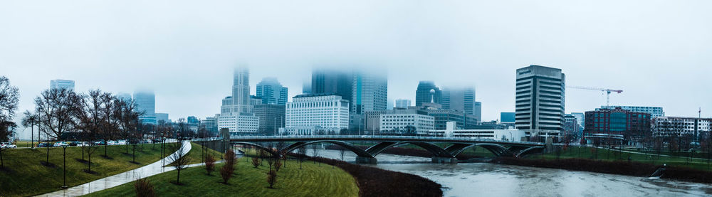 Bridge over river amidst buildings in city against sky