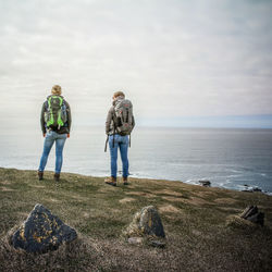 Rear view of hikers standing on hill by sea against cloudy sky