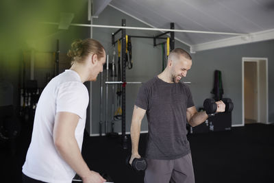 Man exercising with dumbbell with trainer checking his progress