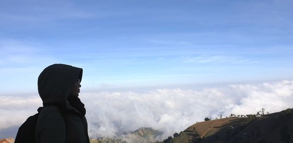 Side view of woman standing on mountain against sky