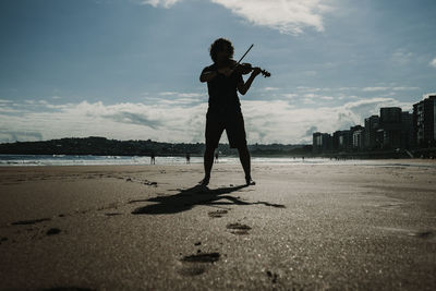 Full length of woman playing violin on beach against sky