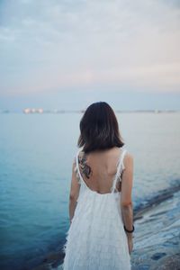 Rear view of woman standing by sea against sky