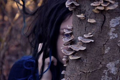 Close-up of woman with leaves on tree trunk