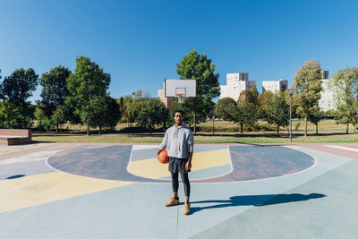 Young sportsman with basketball in sports court on sunny day