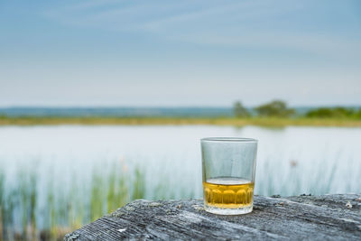 Drink on table by lake against sky