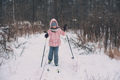 Girl skiing on snow covered field against bare trees