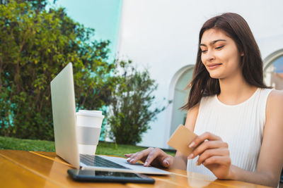 Young woman using phone while sitting on table