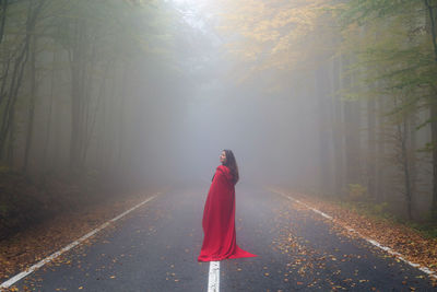 Rear view of woman standing on road in forest during foggy weather