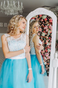 Young woman wearing blue dress reflecting in mirror against flowering plants