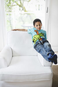Portrait of boy sitting on handrest of armchair at home