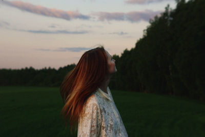 Side view of young woman with long hair standing on land