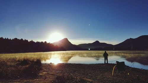 Rear view of silhouette man fishing in lake at sunset