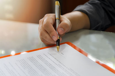 Cropped image of business person signing paper at desk in office
