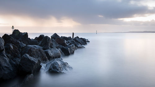 Rocks in sea against sky during sunset