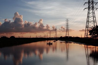 Reflection of electricity pylons against sky on lake during sunset